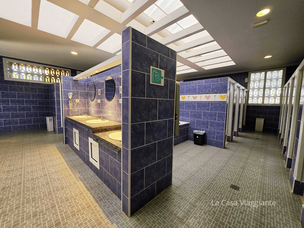 Bagni pubblici con pareti blu, lavabo in granito e cabine separate.